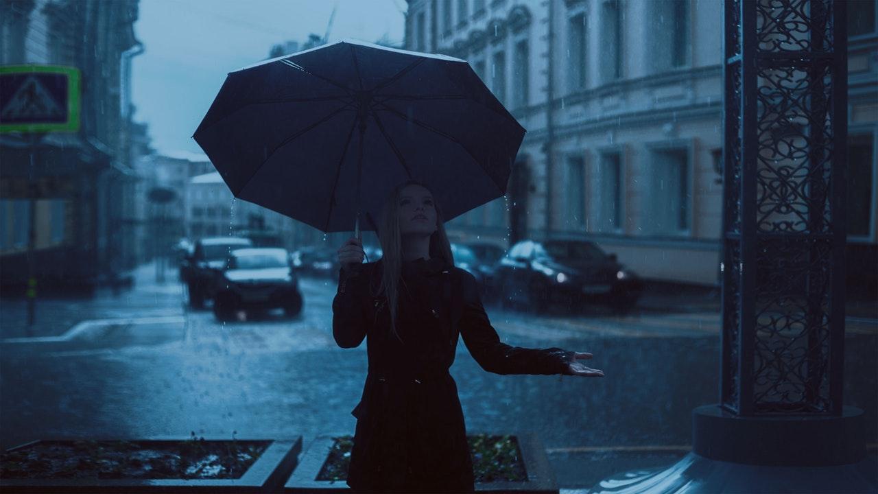 Femeie în ploaie ținând umbrela pe strada unui oraș