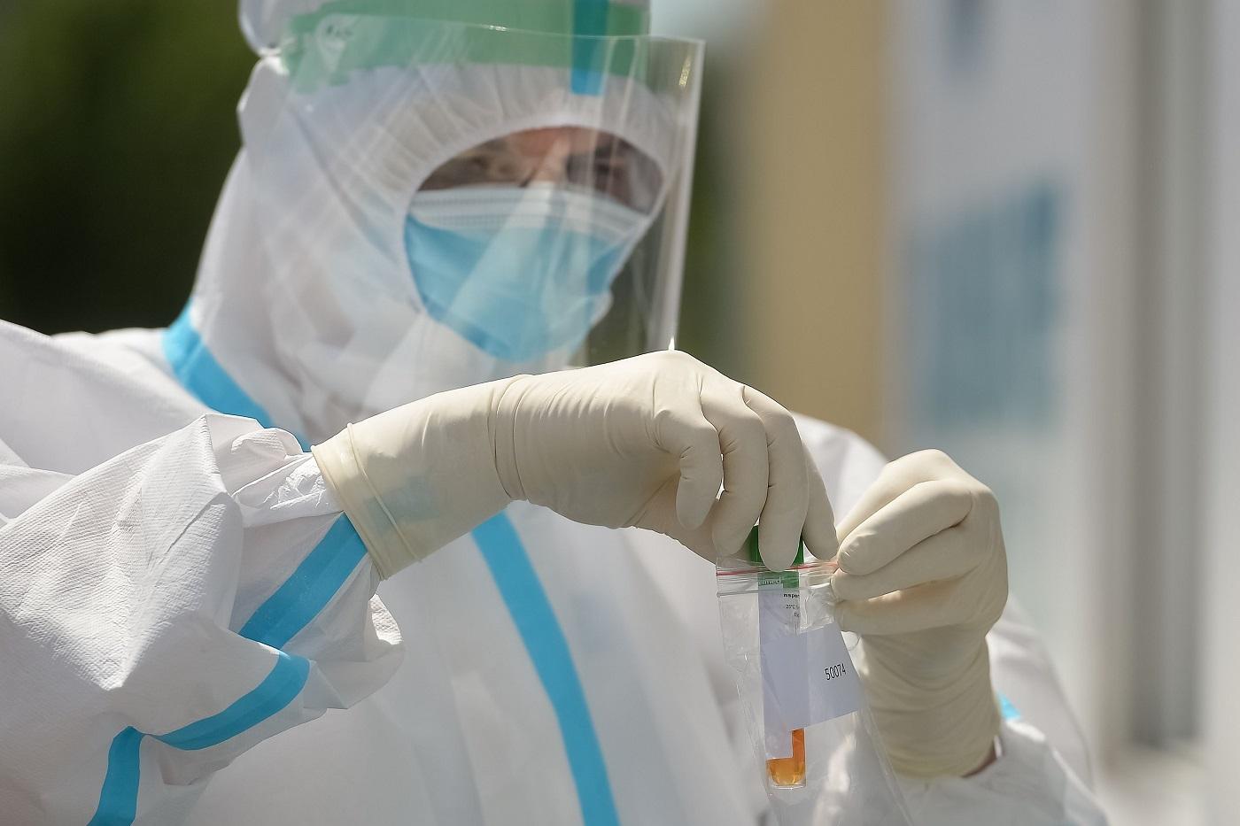 Medic cu combinezon și mască ține în mână probele de test pentru coronavirus