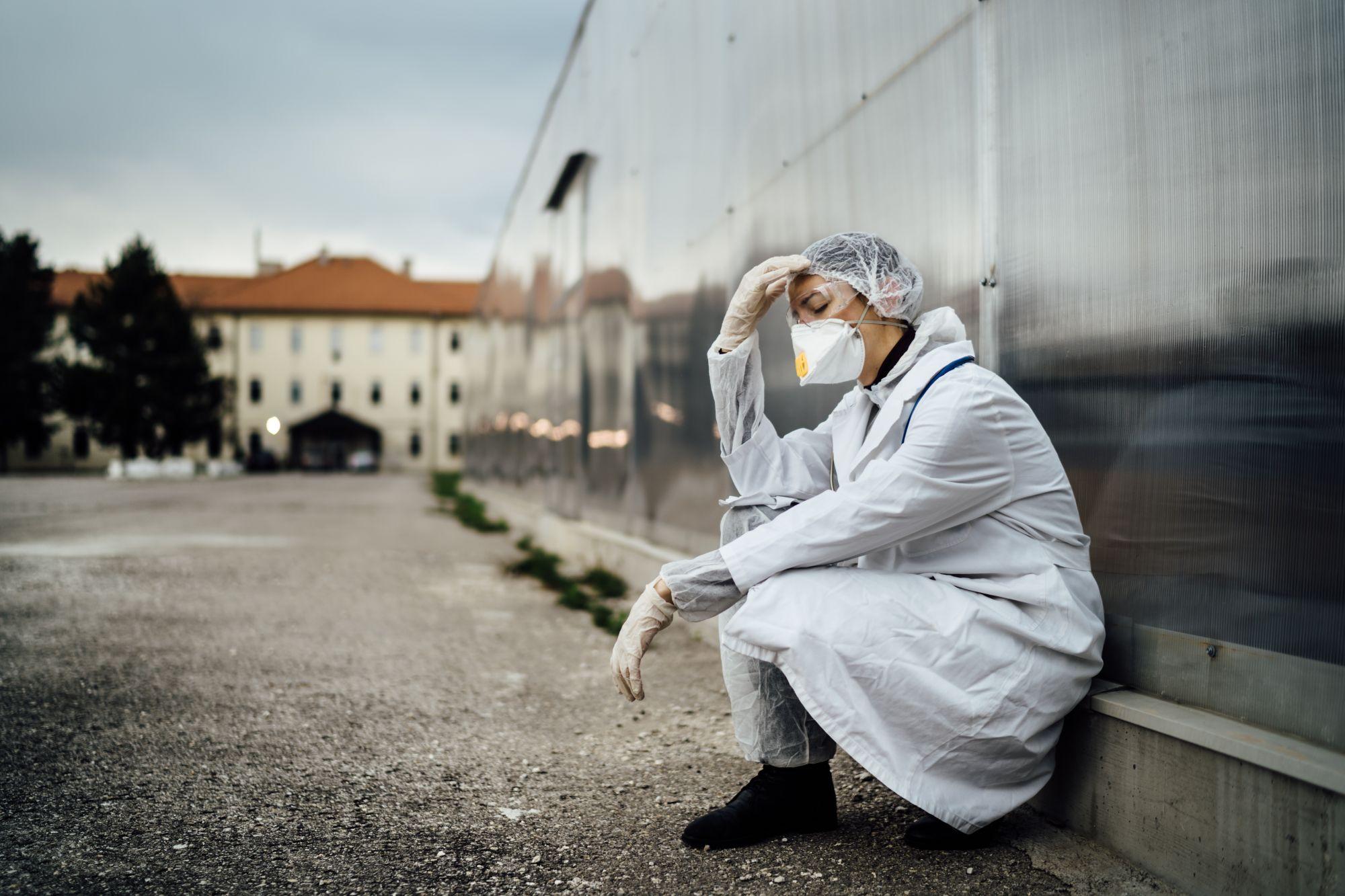 O asistentă stă sprijinită de peretele unui spital, afectată de situaţia pandemică