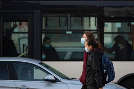 Persoane cu masca de protecţie plimbându-se prin Bucureşti, cu un autobuz pe fundal