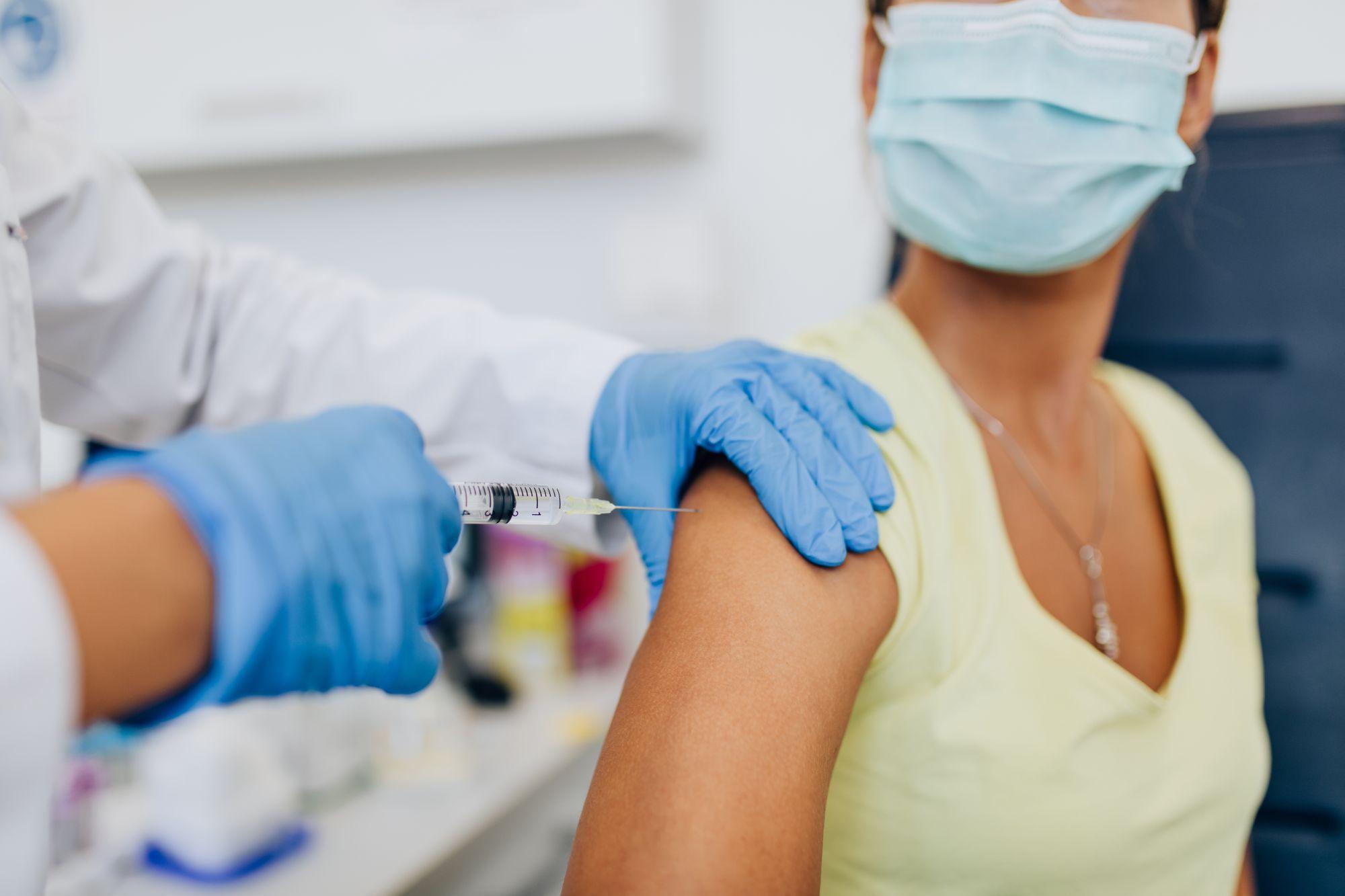 O asistentă administrează un vaccin anti-Covid-19 în umărul unei paciente