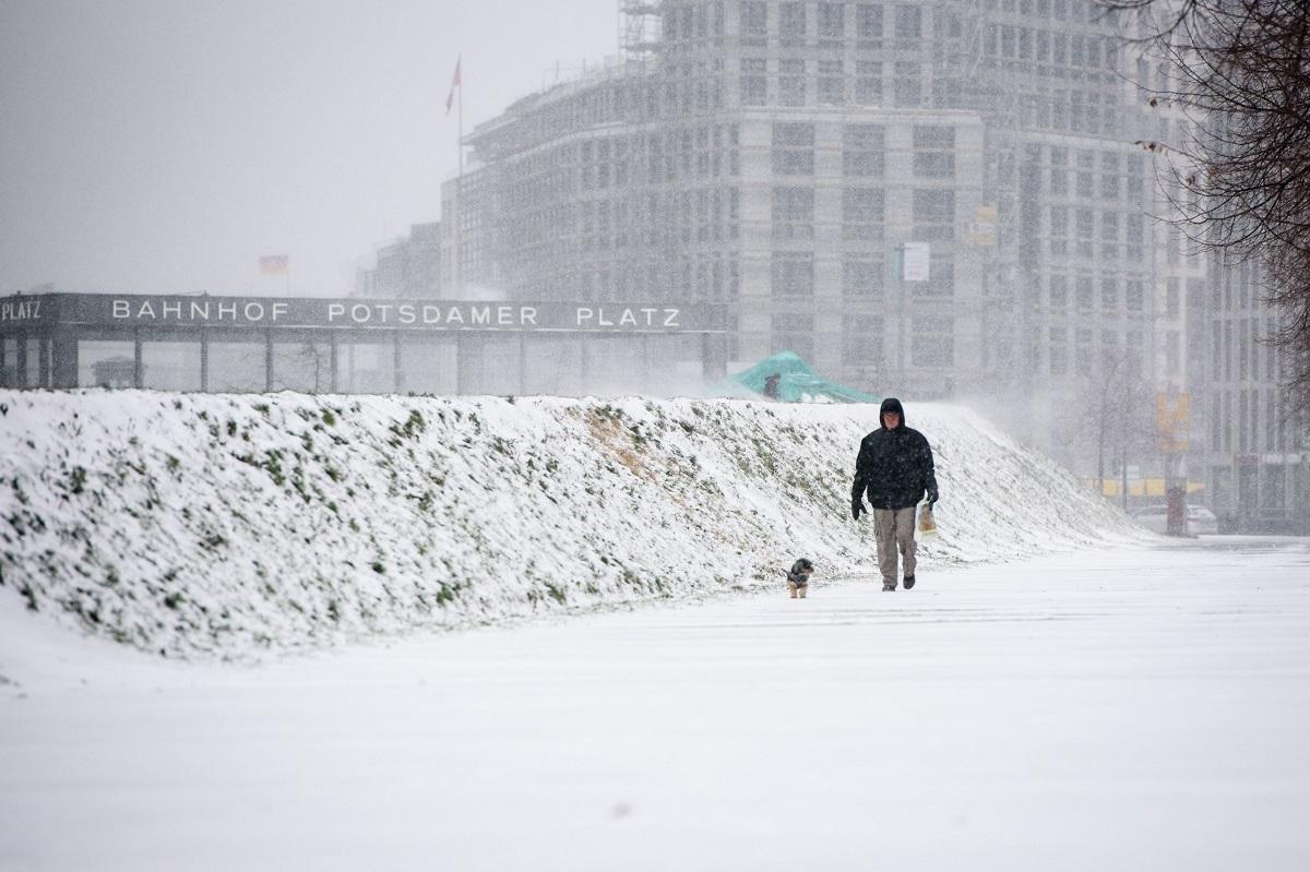 Un bărbat cu câinele său poate fi văzut în timpul ninsorilor în centrul Berlinului