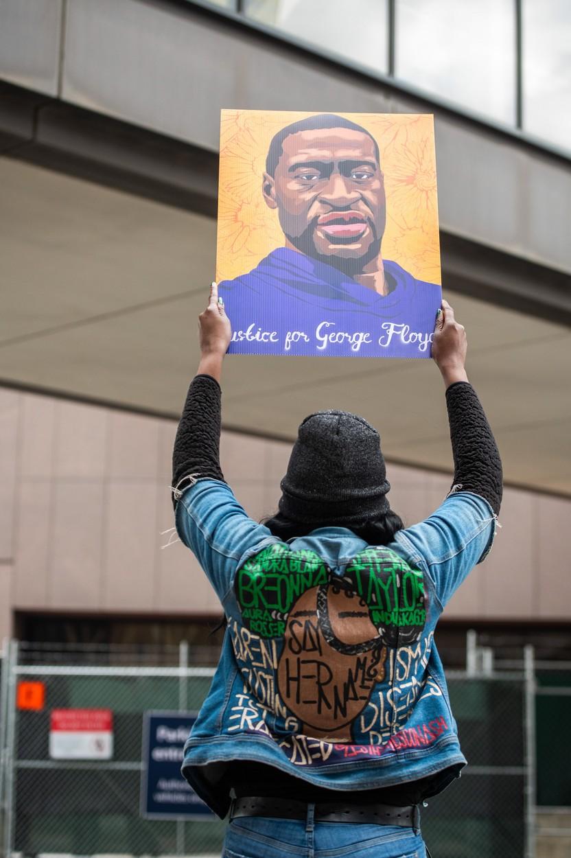 Persoană cu geacă de blugi, ţinând în mâini o pancardă cu George Floyd