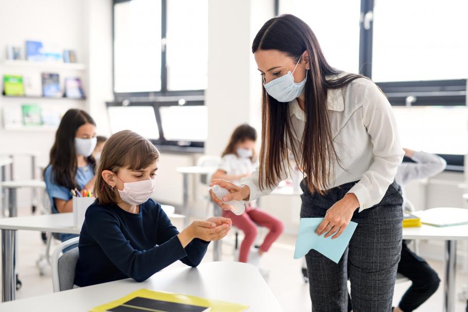 O profesoară ajută elevii să-și dezinfecteze mâinile înainte de începerea examenului O profesoară ajută elevii să-și dezinfecteze mâinile înainte de începerea examenului