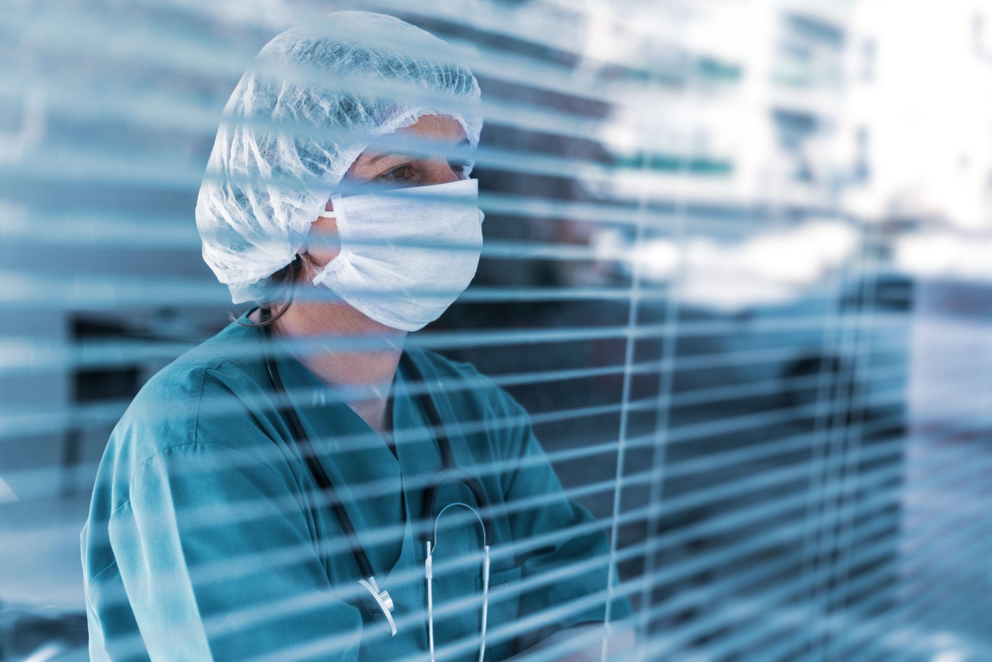 Un doctor priveşte în spatele unui geam de protecţie
