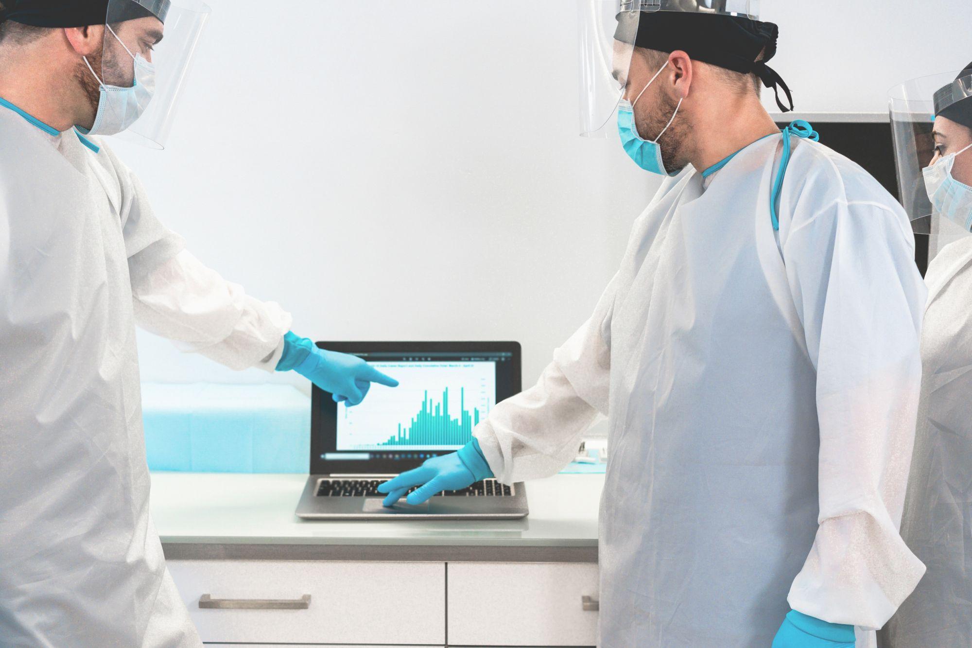 Bilanț coronavirus în România, 28 mai. Personal medical în costume de protecţie uitându-se la un grafic pe laptop