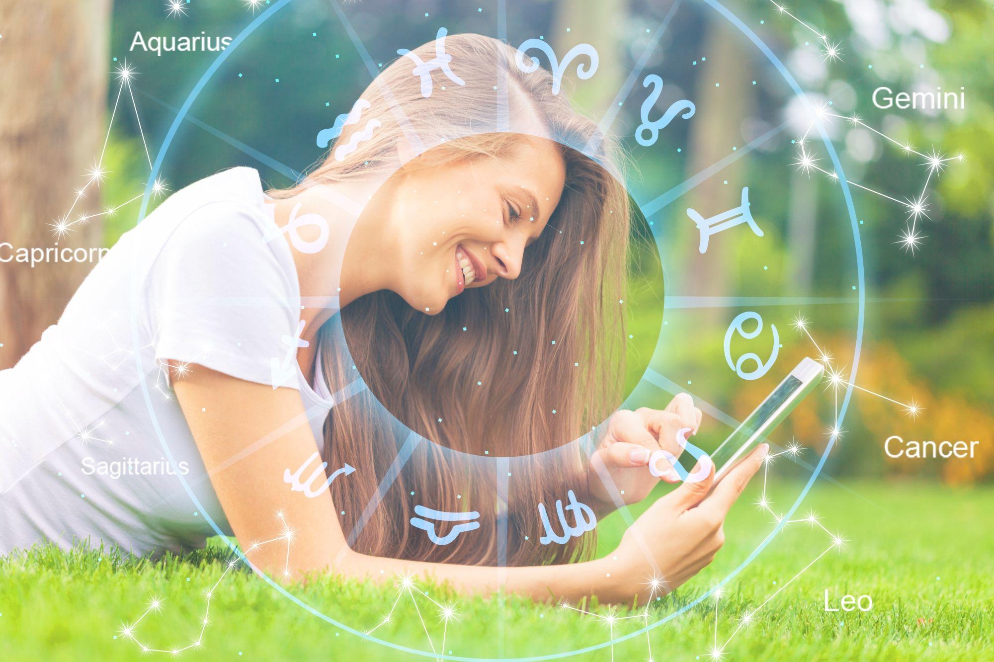 O fată întinsă pe iarbă se uită într-un telefon şi zâmbeşte, pe un fundal cu harta zodiilor