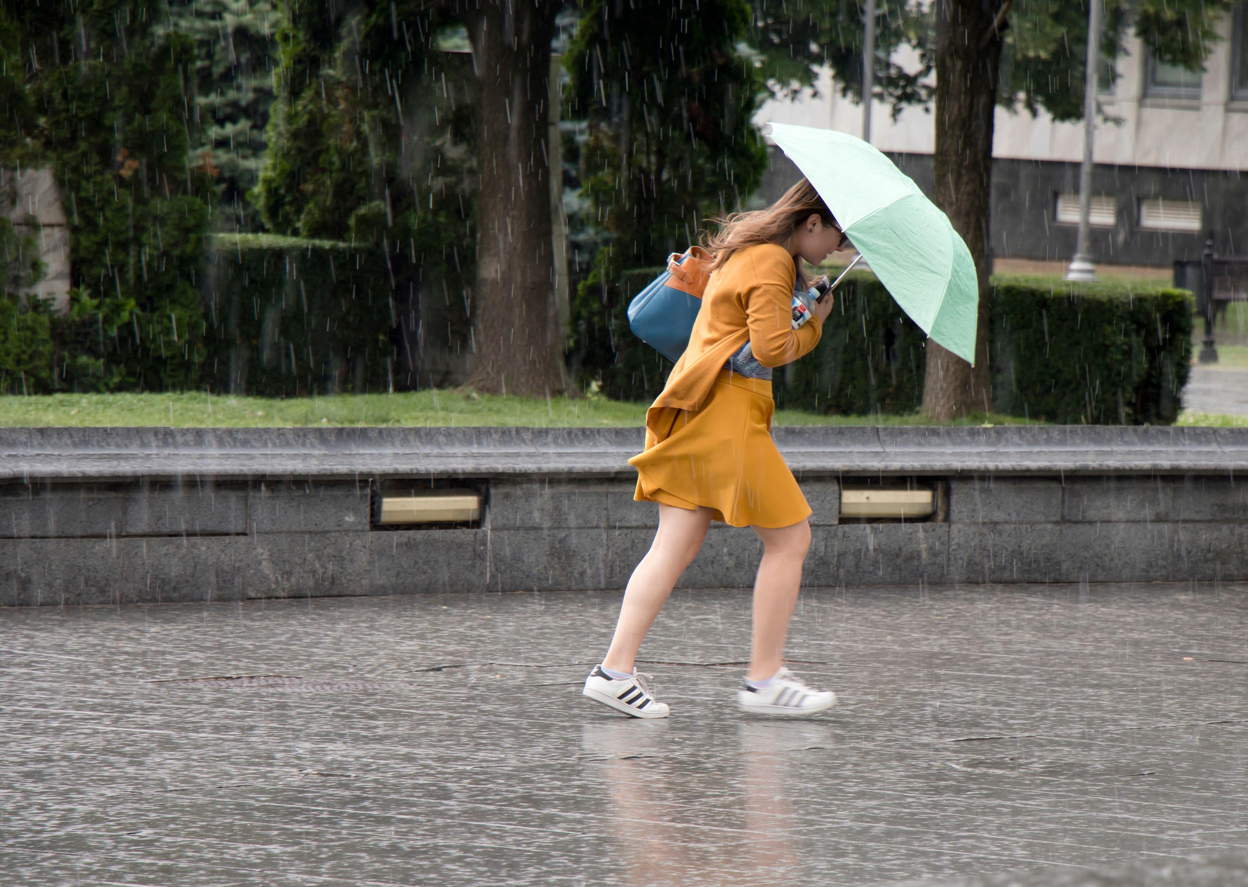 O tânără care aleargă sub umbrelă în ploaia torentială