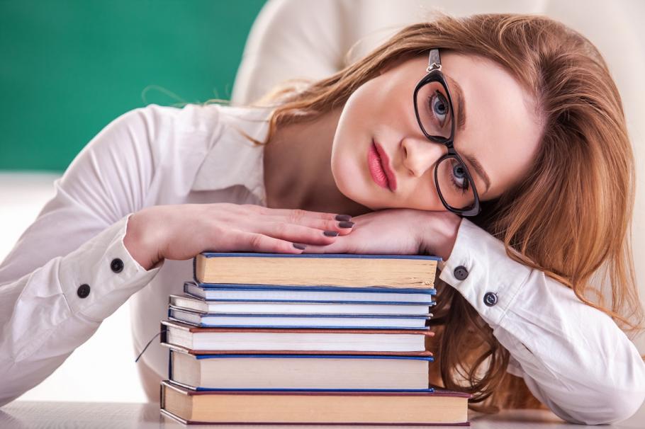 Profesoară În imagine: Profesoară cu ochelari, cu capul sprijinit de câteva cărţi aşezate pe masă