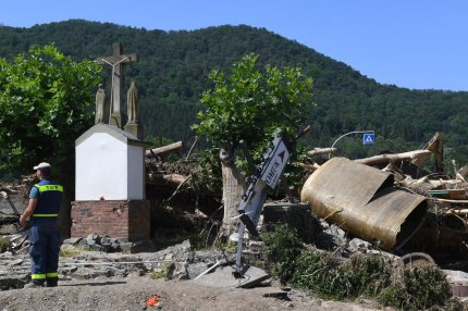 Un muncitor stă lângă o cruce de la marginea drumului, într-o zonă devastată de inundații