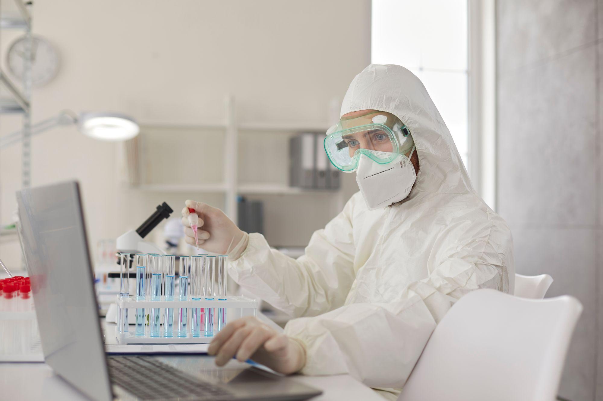 Bilanț coronavirus în România, 1 septembrie. Om de ştiinţă într-un laborator, analizând probe şi lucrând la un laptop, în costum de protecţie