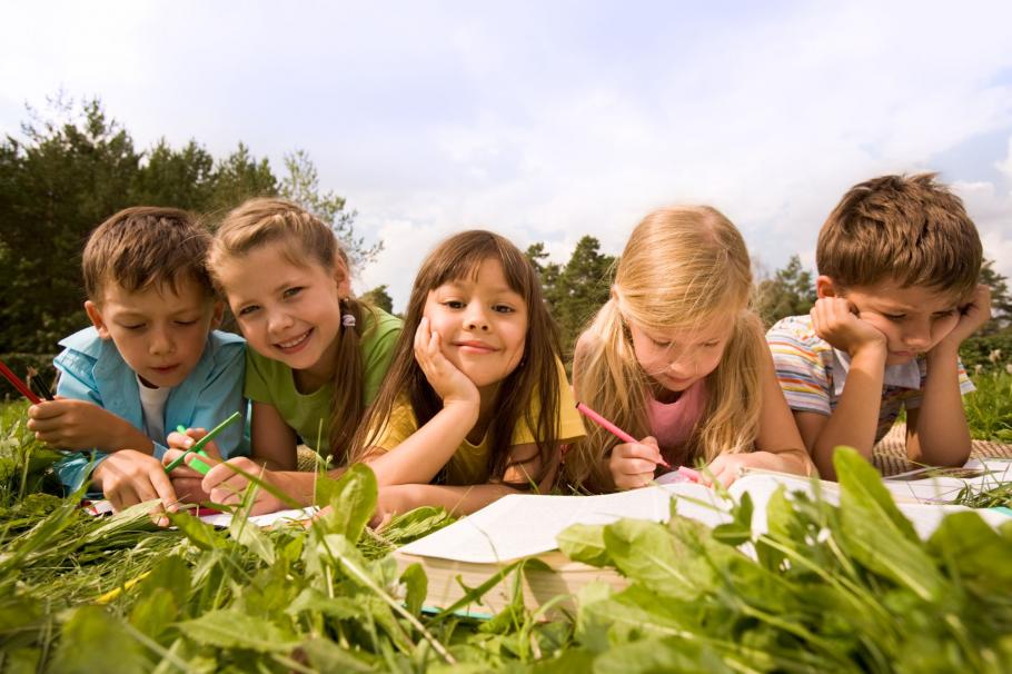 Copii învăţând pentru şcoală întinşi pe iarbă