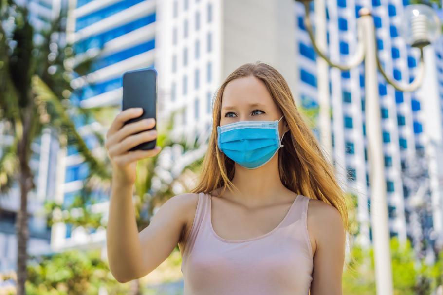 Apple a lansat iOS 15.4 O femeie se uită la telefon cu masca de protecţie pe faţă