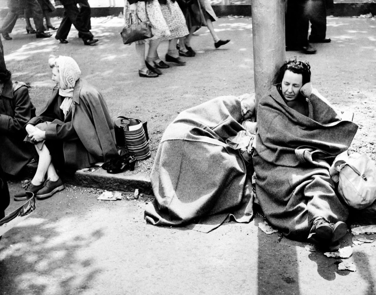Femei dormind pe marginea străzii, la 1 iunie 1953, în timp ce așteaptă pe ruta regală în ajunul încoronării Reginei Elisabeta a II-a a Marii Britanii