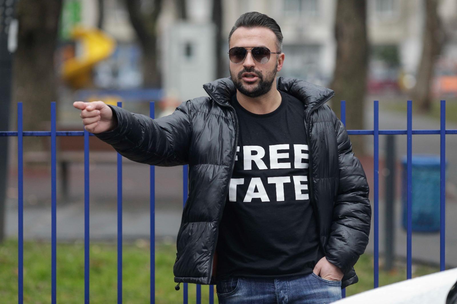 Fraţii Tate, legaţi amândoi cu o pereche de cătuşe, au stat 5 ore la tribunal. Mesajul afişat de un susţinător