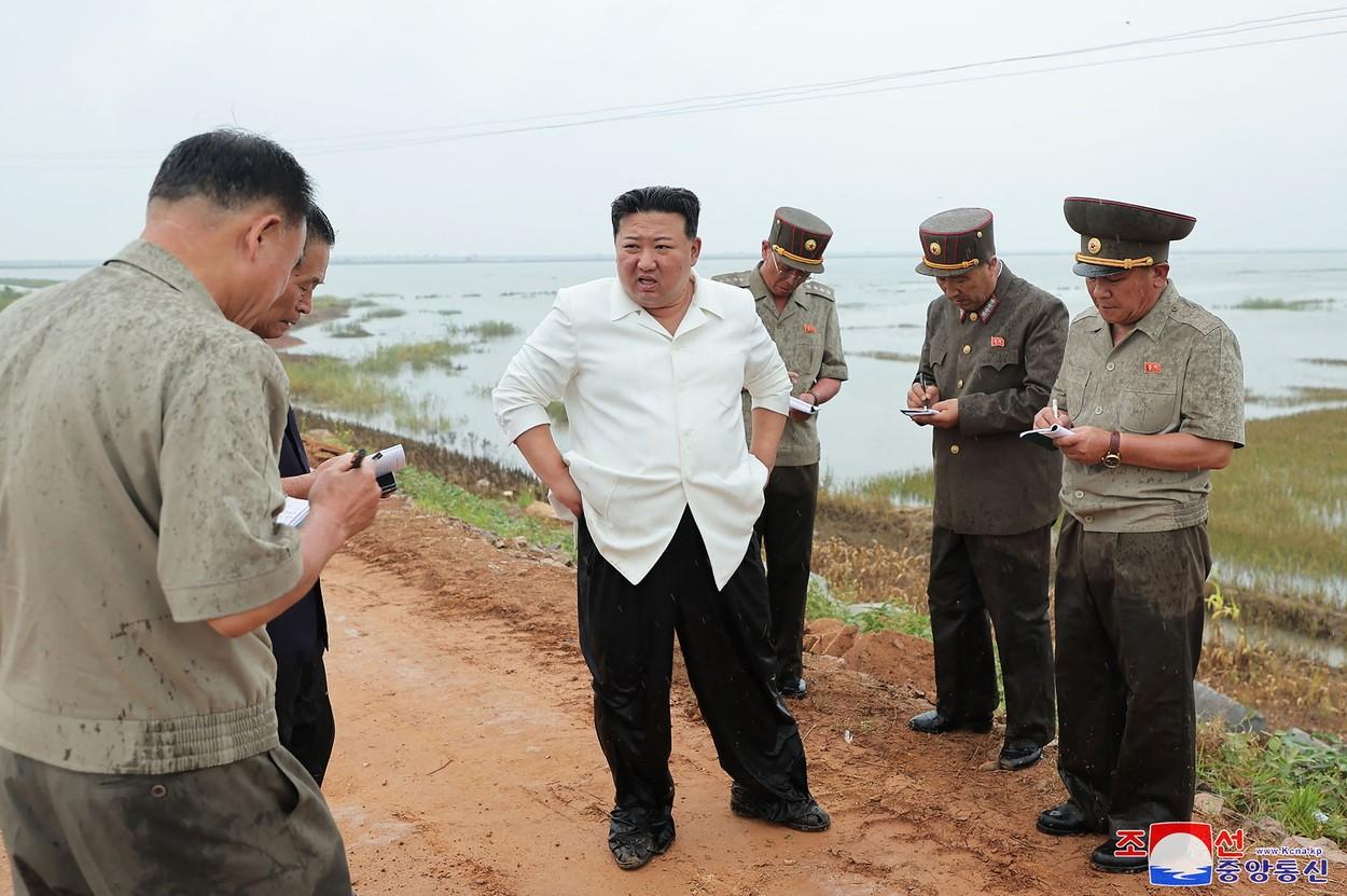Kim Jong Un, furios, în apă până la genunchi, într-un câmp de orez, inundat, critică gruvernul iresponsabil. Oficialii iau notiţe lângă el