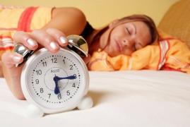 Tânără care doarne cu mâna pe ceasul deșteptător