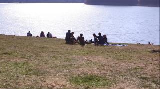 Oameni stau la soare pe vreme frumoasă, lângă lac