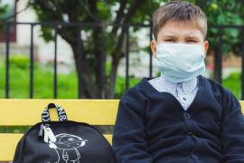 Copil cu mască de protecţie, stând pe o bancă