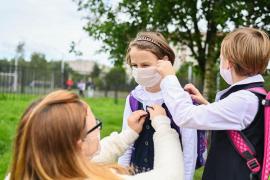 O mamă aranjează ținuta copiilor ei, care include și masca de protecție