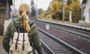 Femeie cu părul blond, prins în coadă, pe peronul gării