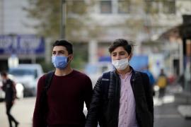 Doi adolescenți poartă mască de protecție, pe stradă.