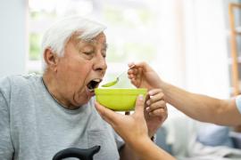 Un bătrân este hrănit de un îngrijitor