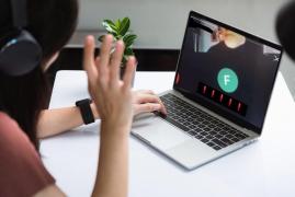 O elevă se uită la monitorul unui laptop în timp ce un profesor vorbește, în timpul orelor online