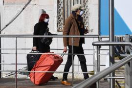 Două persoane cu măşti de protecţie la gură se îndreaptă cu geamantanele către aeroport