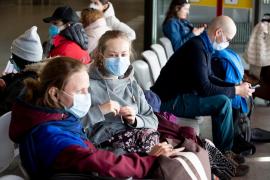 Călători cu măști la gură așteptând pe scaune, în aeroport