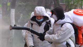 Bărbat în combinezon dezinfectează strada cu o instalație