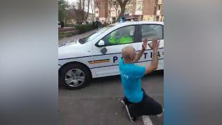 Localnic în genunchi lângă mașina de poliție