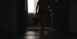 O fată pășește într-o cameră întunecată cu un ursuleț în mână