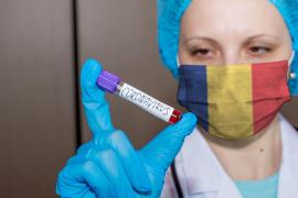 O asistentă care poartă o mască de protecţie în culorile drapelului României ţine o fiolă marcată cu coronavirus