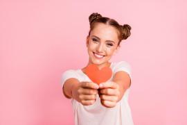 O femeie zâmbeşte şi ţine în mâini o inimă din carton roşu