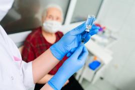 Un doctor cu mănuși pregătește vaccinul anti-coronavirus pentru o femeie în vârstă