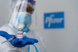 Un lucrător medical prezintă un vaccin, pe fundalul firmei Pfizer