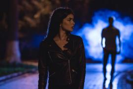 O femeie pe o stradă întunecată noaptea, având în spate un bărbat