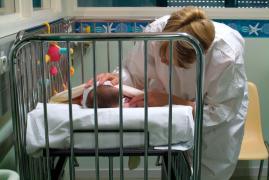 O femeie stă lângă patul unui nou-născut