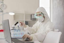 Om de ştiinţă într-un laborator, analizând probe şi lucrând la un laptop, în costum de protecţie