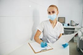 O doctoriţă cu mască de protecţie stă pe scaun şi notează într-un raport