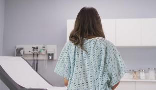 Femeie stând cu spatele pe un pat de spital