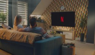 Un cuplu stă aşezat pe canapea şi se uită pe Netflix. Platforma a anunţat o nouă scumpire a abonamentelor