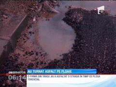 Pe o ploaie torenţială, printre maşini şi bălţi, o echipă de muncitori a turnat asfalt pe o stradă din Târgu Jiu
