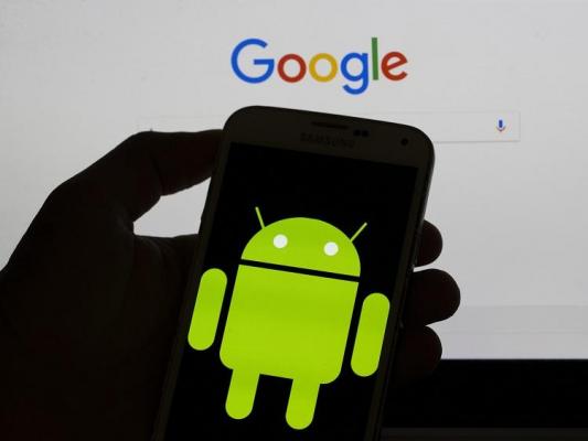 Logo-ul Android afişat pe un smartphone, în faţa unui monitor cu Google Search