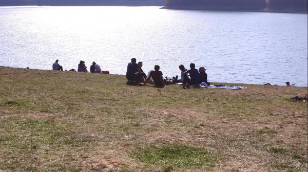 Oameni stau la soare pe vreme frumoasă, lângă lac