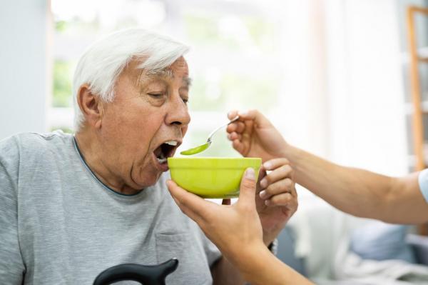 Un bătrân este hrănit de un îngrijitor