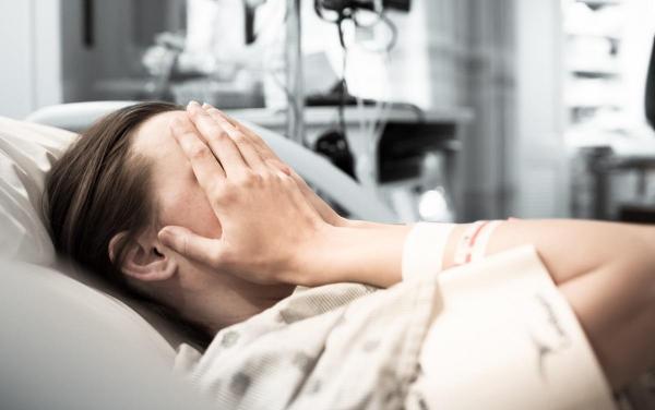 Femeie pe patul de spital cu mâinile pe faţă