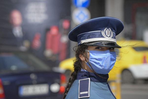 Un agent de politie ce poarta o masca de protectie priveste spre camera de filmat