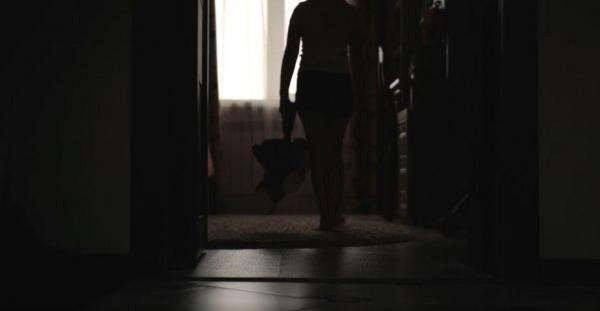 O fată pășește într-o cameră întunecată cu un ursuleț în mână